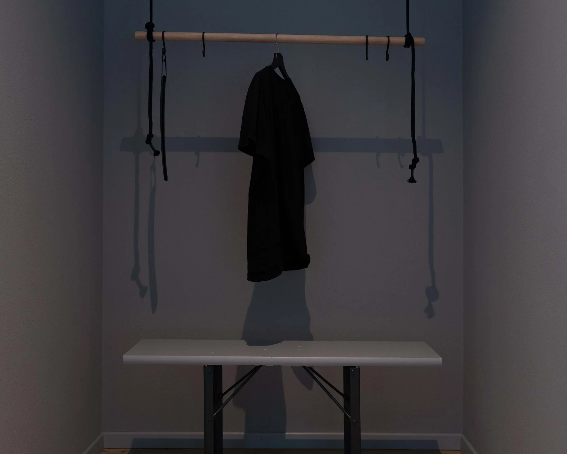 Impressionen aus dem Luis von Weyden Schwarzes Kleidungsstück hängt an Holzstange über weißer Bank in dunklem Raum