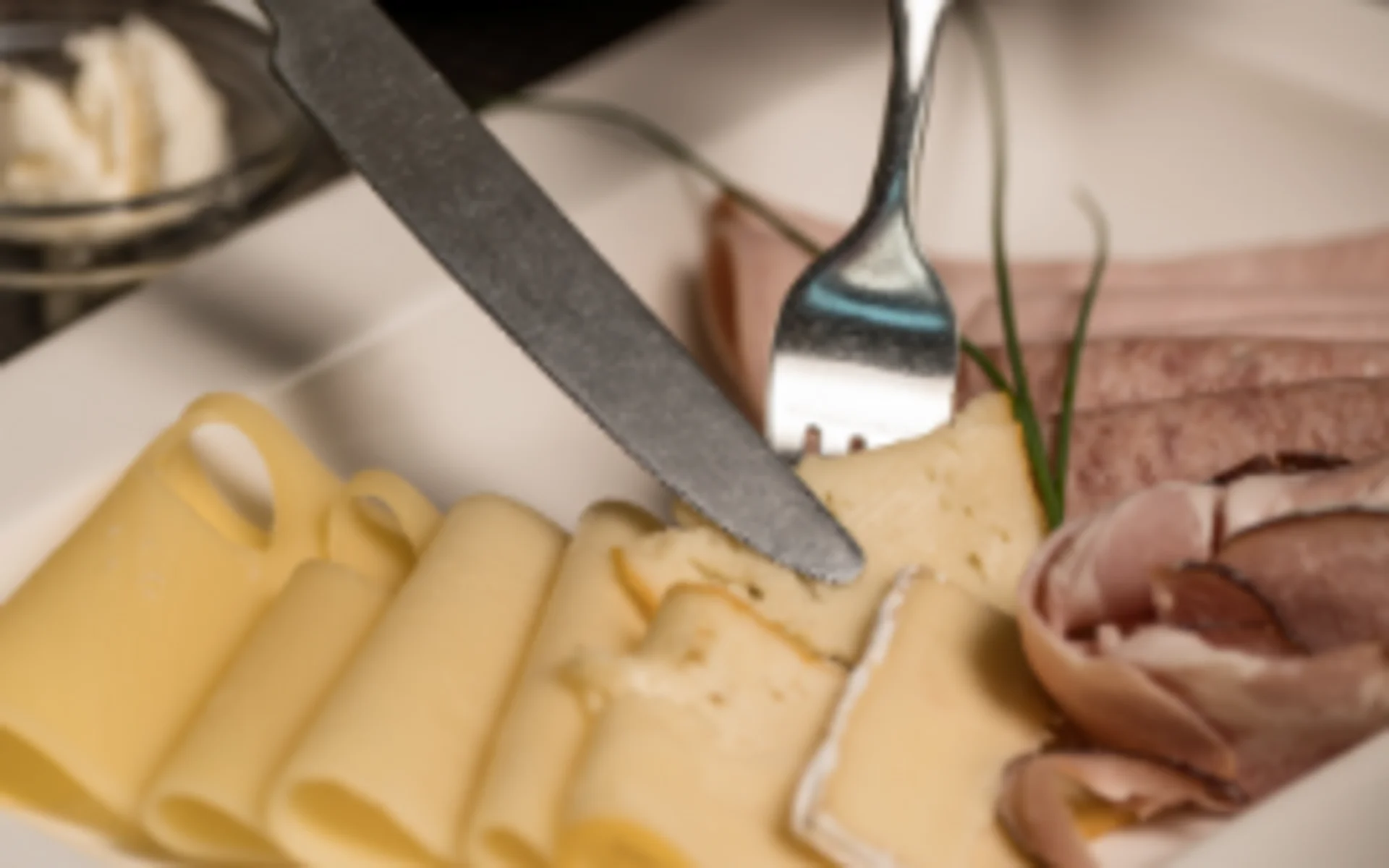 Luis von Weyden: Frühstück in Weiden am See Person schneidet Käse auf Teller mit Wurst und Brot im Hintergrund