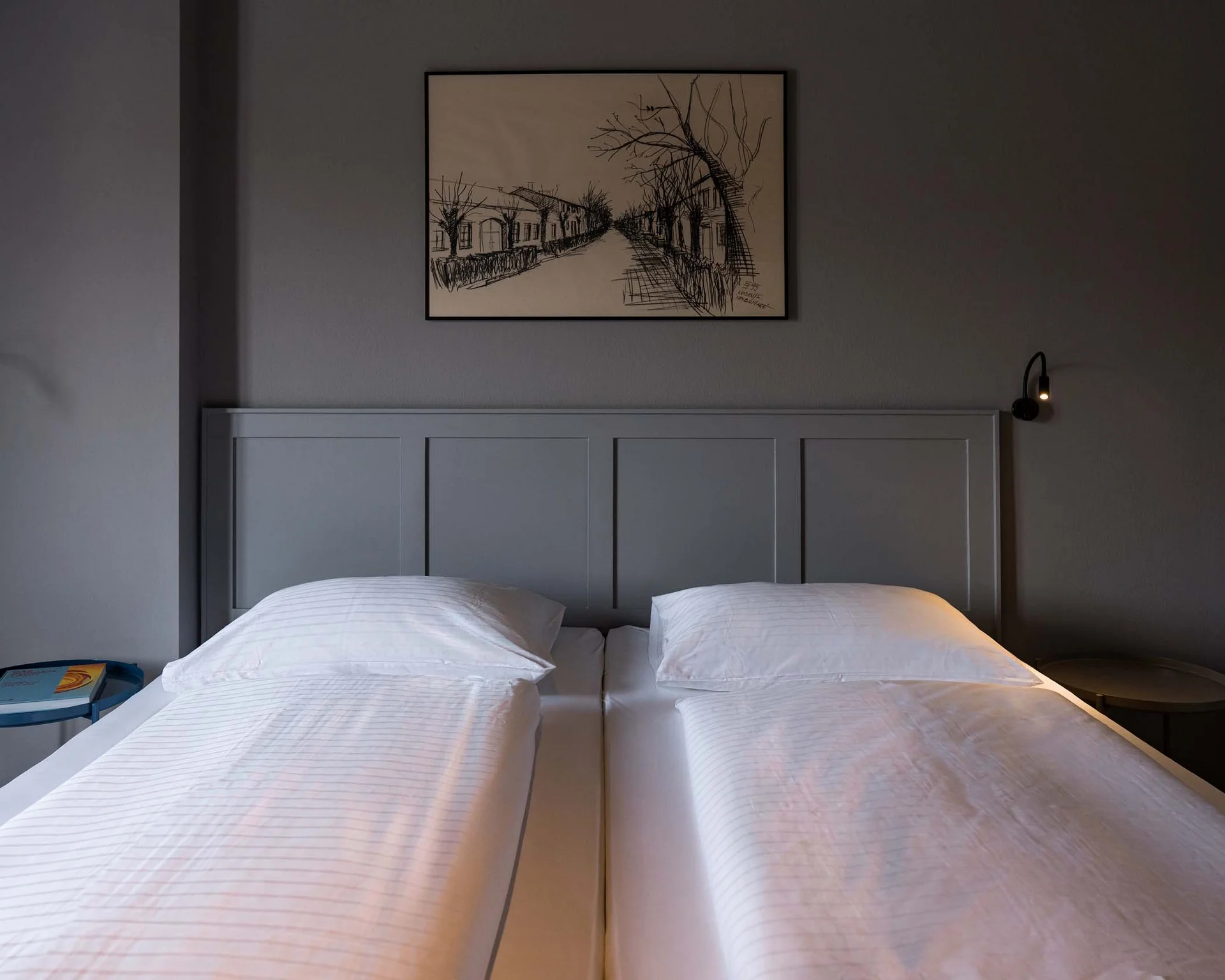 Impressionen aus dem Luis von Weyden Zweibettzimmer mit weißen Betten, grauer Wand und schwarzem Wandbild