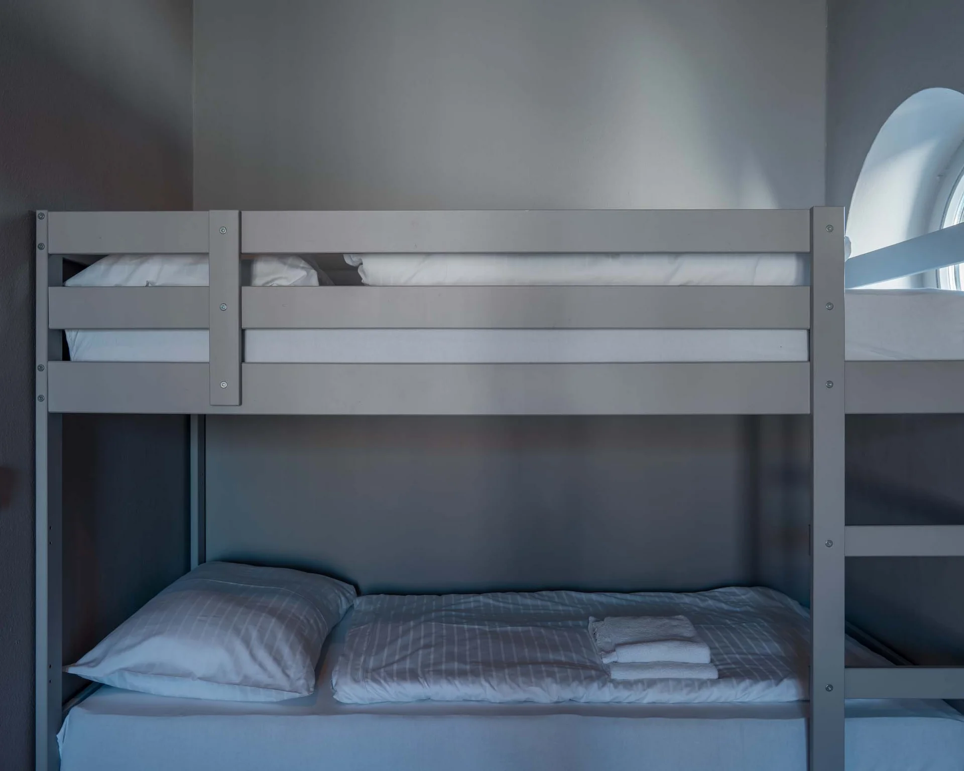 Impressionen aus dem Luis von Weyden Graues Etagenbett in einem schlichten, grauen Zimmer mit rundem Fenster