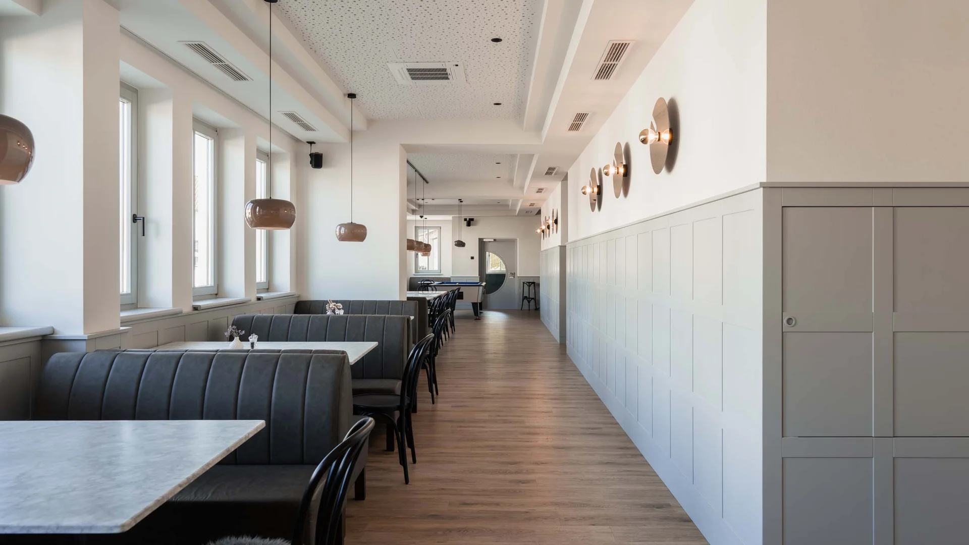 Luis von Weyden: die stylishe Pension in Weiden am See Moderner, leerer Gastronomiebereich mit grauen Sitzbänken und hölzernem Boden